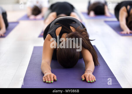 Frau und eine Gruppe junger sportliche Menschen üben Yoga Lektion, Kind, Balasana darstellen, Innen- Sitzung zu schließen, der die Teilnehmer bei der Arbeit Stockfoto