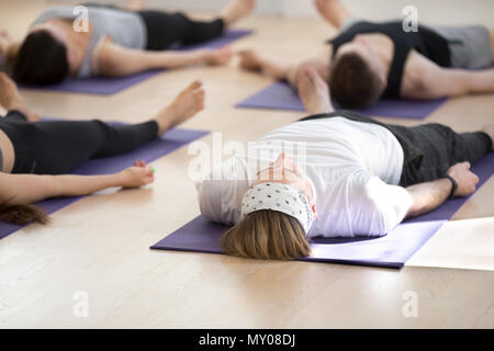 Gruppe junge sportliche Menschen üben Yoga Lektion, Savasana darstellen, Leiche, toten Körper trainieren, trainieren, Hallenbad in voller Länge, Studenten Training". Stockfoto