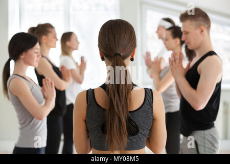 Gruppe junge sportliche Menschen üben Yoga mit Instruktor, entspannen Sie sich nach der Lektion oder ab Klasse, Meditation, Namaste darstellen, Indoor cl Stockfoto