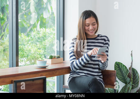 Gerne Asien Frau mit Handy in der Nähe der Fenster im Cafe Restaurant, digitalen Zeitalter casual lifestyle, Leben außerhalb Home Konzept Stockfoto