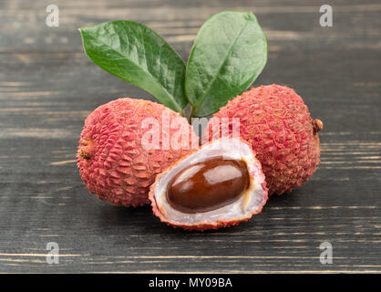 Zwei lychee Obst in der Shell mit der Hälfte und Blätter auf Holz- Hintergrund Stockfoto