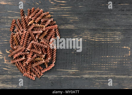 Kleine dunkle Haufen von Pasta Fusilli auf leeren Holz- Hintergrund Stockfoto