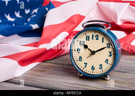 USA-Flagge und Wecker. Zerknitterte Flagge der Vereinigten Staaten von Amerika und Mechanischer Wecker auf Holz- Oberfläche schließen. Stockfoto