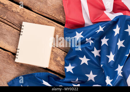 Zerknitterte amerikanische Flagge und Notebook. Rüschen USA satin Flagge und leeres Papier notepad auf rustikalen hölzernen Brettern. Stockfoto