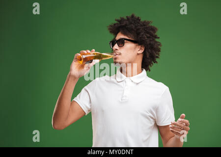 Bild der hübschen jungen afrikanischen curly Mann über grüne Wand Hintergrund Bier trinken isoliert. Stockfoto