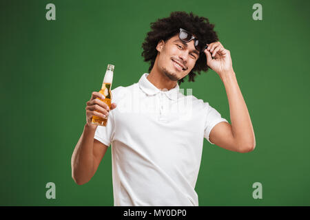 Bild der hübschen jungen afrikanischen curly Mann über grüne Wand Hintergrund Bier trinken isoliert. Stockfoto