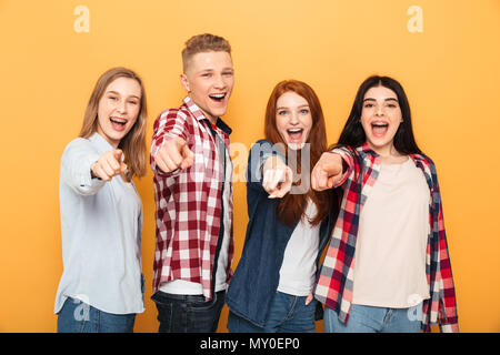 Gruppe von Happy school Freunde Pointing Finger an der Kamera, während zusammen, die auf gelbem Hintergrund Stockfoto