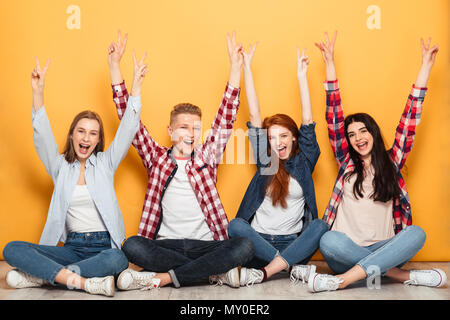 Gruppe von Jugendlichen positiv Schule Freunde sitzen mit den Händen über Gelb Hintergrund angehoben Stockfoto