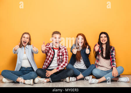 Gruppe von Jugendlichen positiv Schule Freunde sitzen und mit Daumen nach oben Geste auf gelbem Hintergrund Stockfoto