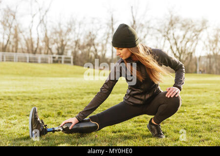 Bild von brunette deaktiviert sportliche Mädchen in Sportkleidung Sport und Stretching Beinprothese auf Gras Stockfoto