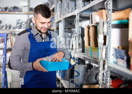 Junge lächelnde positiver Mann Arbeiter gehen durch Sanitärtechnik Details in der Werkstatt Stockfoto