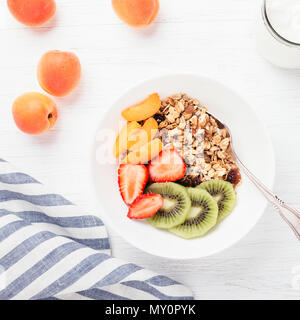 Gesundes Frühstück. Die Schüssel Müsli mit frischen Früchten und griechischer Joghurt auf die weiße Holztisch. Ansicht von oben, Quadrat Bild. Auf dem Tisch. Stockfoto