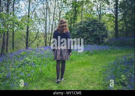 Eine junge Frau wird zu Fuß in einem Wald mit Glockenblumen Stockfoto