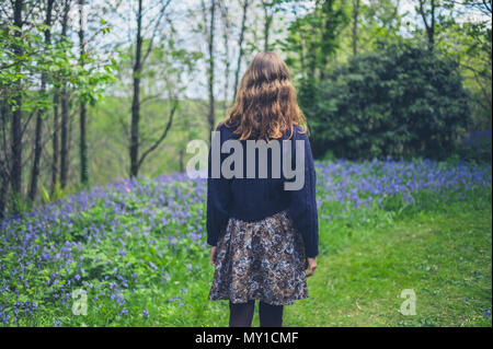 Eine junge Frau wird zu Fuß in einem Wald mit Glockenblumen Stockfoto