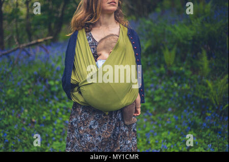 Eine junge Mutter mit Baby steht auf einer Wiese der bluebells Stockfoto