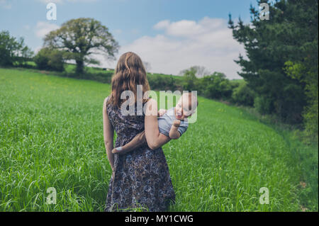 Ein glückliches Baby von seiner Mutter in einem Feld gehalten wird, ist dabei eine Faust Pumpe Stockfoto