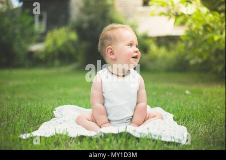 Ein süßes kleines Baby sitzt auf dem Gras draußen im Park Stockfoto