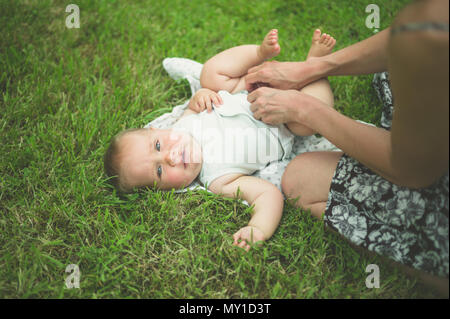 Eine junge Mutter verändert sich Windel ist ihr Baby auf dem Gras in der Natur Stockfoto