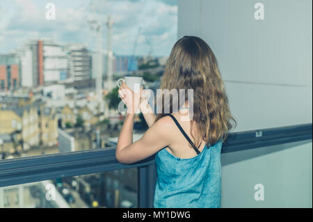 Eine junge Frau trinkt eine Tasse Kaffee auf Ihrem Balkon in der Stadt Stockfoto