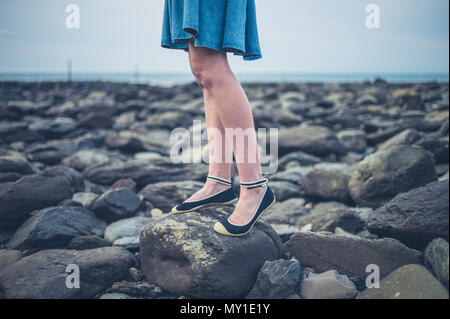 Die Füße und die Beine einer jungen Frau trägt einen Rock stehen auf dem Strand im Herbst Stockfoto