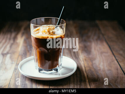Schwarz Eiskaffee in einem hohen Glas mit einem Stroh auf einem rustikalen Holztisch Stockfoto