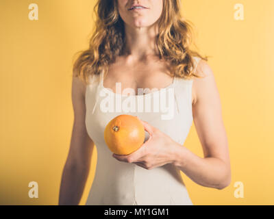 Eine junge Frau steht vor einem gelben Hintergrund Holding eine Grapefruit Stockfoto