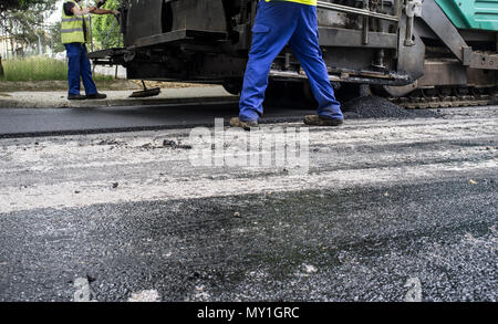 Die Arbeit an der Festlegung von Asphalt in der Stadt. Pflasterung Applikator Maschine oder Fertiger mit Arbeitern Stockfoto