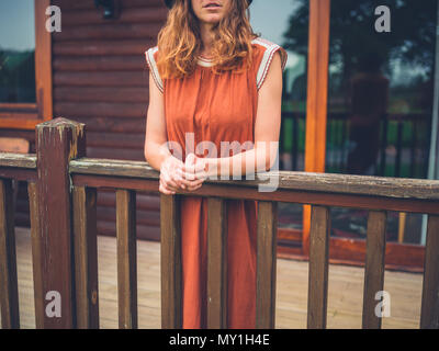 Eine junge Frau trägt ein Kleid steht auf der Veranda eines Blockhaus Stockfoto