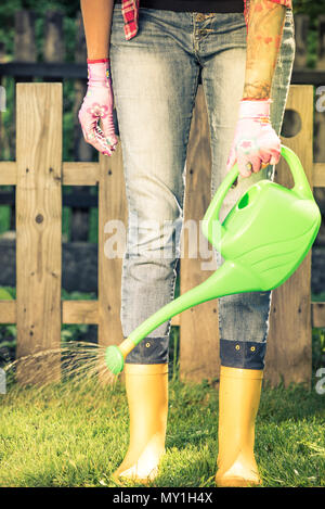 Tätowierte Frau watring Pflanzen im Garten tragen Gummistiefel. Stockfoto