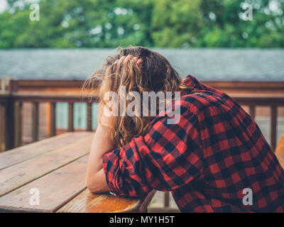 Eine traurige, müde Junge Frau sitzt auf der Veranda eines Blockhaus Stockfoto