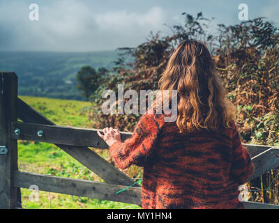 Eine junge Frau steht durch einen Zaun und Tor in der Landschaft Stockfoto