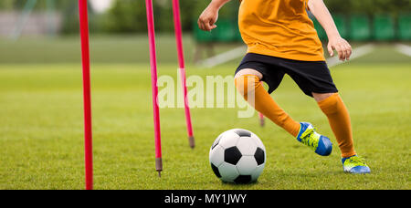 Fußball-Spieler mit Ball laufen Slalom um Ausbildung Sticks. Das Fußball-Training. Junge Fußballer in Gelb Sportswear am Training Sessi Stockfoto