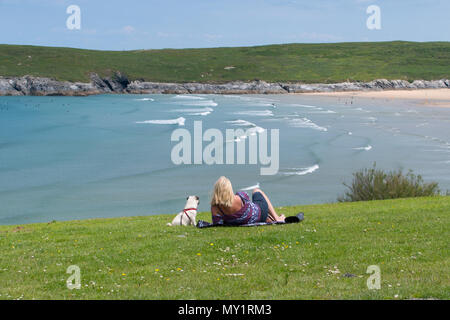 Frau und ihr Hund sitzen/auf dem Gras in Richtung Meer und Crantock Beach in Cornwall auf der Suche liegen Stockfoto