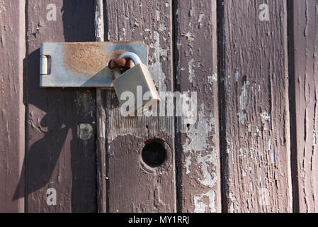 Ein altes Holz Tür mit gerissenen und blättert die Farbe von einem Messing Vorhängeschloss gesichert Stockfoto