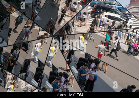 Der Eingang aus Glas in ein Einkaufszentrum in Harajuku, Tokio, spiegelt Menschen vorbei in die Straße vor dem Gebäude. Stockfoto