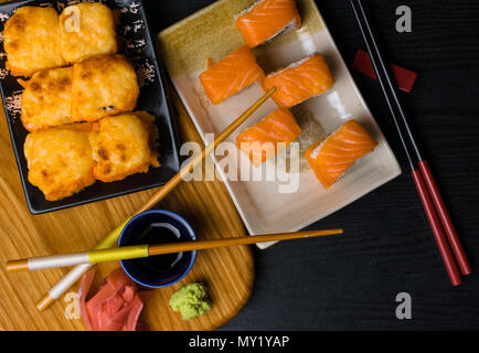 Mischung von Sushi mit Käse, Lachs, Garnelen, Avokado, Gurke. Japan Essen mit Stäbchen, Ingwer, Wasabi, soy souce auf Holzbrett. Sushi Menü Stockfoto