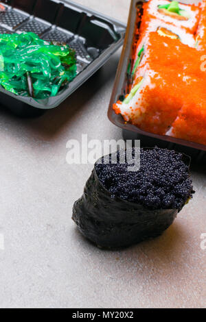 Red Sushi mit Lachs, orange Kaviar, Gurke, Avokado und Schwarz gunkan mit grünen Algen auf grauen Hintergrund. Japan Food Stockfoto