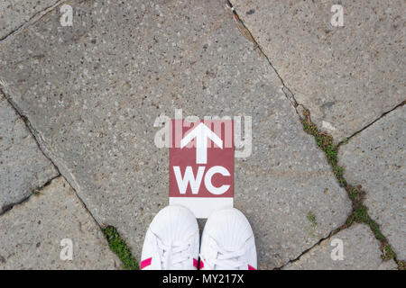 Selfie der Füße Schuhe stehen auf dem Estrich mit wc wc Symbol auf der Straße. Freier Platz für Text. Konzept: Entscheidungen treffen. Stockfoto