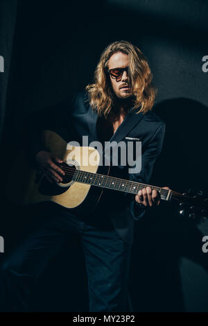 Schöne stilvolle Mann in Anzug und Sonnenbrille Gitarre spielen auf Schwarz Stockfoto