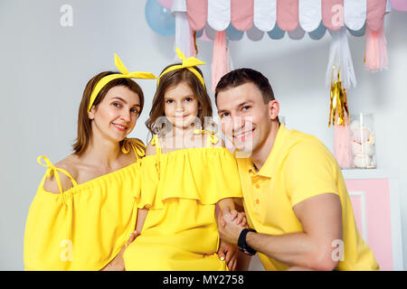 Mama, Papa Umarmungen Tochter, sitzen auf großen makronen vor dem Hintergrund der weißen Wand und Candy Bar im Studio. Gefühle des Glücks. Glückliche Familie po Stockfoto