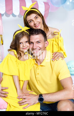 Mama, Papa Umarmungen Tochter, sitzen auf großen makronen vor dem Hintergrund der weißen Wand und Candy Bar im Studio. Gefühle des Glücks. Glückliche Familie po Stockfoto