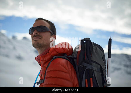 Porträt eines westlichen Menschen im Winter Mantel trägt einen Rucksack und Sonnenbrille hoch oben in den Bergen Stockfoto