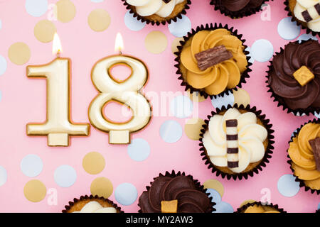 Nummer 18 gold Kerze mit Cupcakes gegen ein Pastell rosa Hintergrund Stockfoto