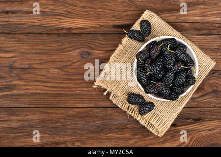 Maulbeeren in einer Schüssel auf einem Sack und in der leere Holz- Hintergrund Stockfoto