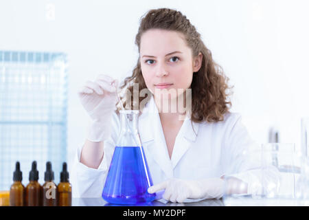 Wissenschaftlerin rühren eine blaue Mischung in einem Labor Kolben mit einem Glasstab während der pharmazeutischen Medizin test Stockfoto