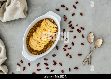 Blick von oben auf ein süßes raw Ernährung Obst Dessert mit Schichten von Apple, Goji Beeren um und zwei Teelöffel auf einem grauen Counter verstreut Stockfoto