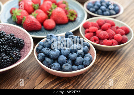 Verschiedene frische Sommer Beeren in Schalen auf hölzernen Hintergrund closeup Stockfoto