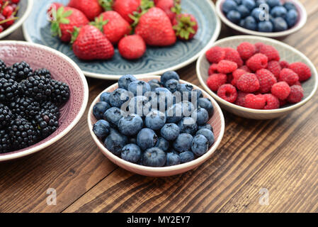 Verschiedene frische Sommer Beeren in Schalen auf hölzernen Hintergrund closeup Stockfoto