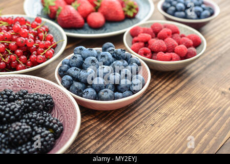 Verschiedene frische Sommer Beeren in Schalen auf hölzernen Hintergrund closeup Stockfoto