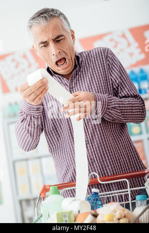 Mann tut Lebensmittelgeschäft Einkaufen im Supermarkt und die Überprüfung einer lange teuren Quittung, ist er schockiert und keuchend Stockfoto